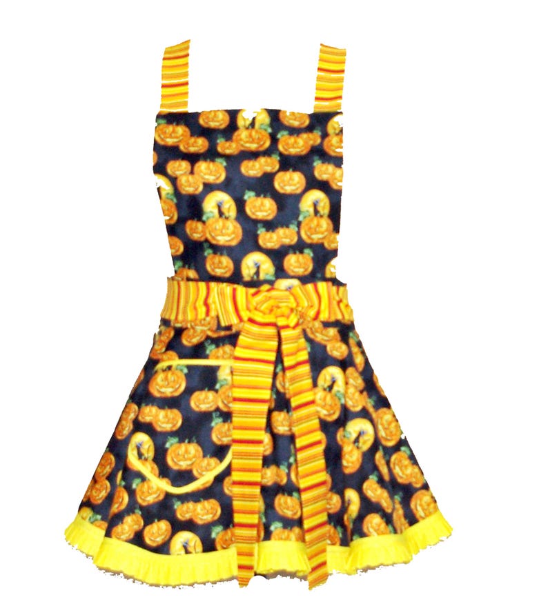 Puede incluir: Un delantal negro y amarillo con estampado de calabaza. El delantal tiene una corbata a rayas amarilla y roja y un volante amarillo alrededor del borde inferior.