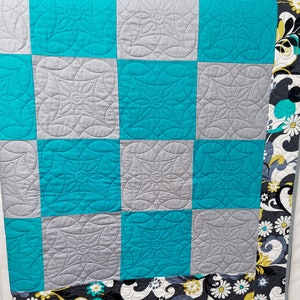 May include: A turquoise and gray patchwork quilt with a floral print border. The quilt is made of squares with a quilted design.