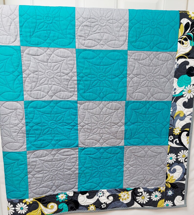 May include: A turquoise and gray patchwork quilt with a floral print border. The quilt is made of squares with a quilted design.