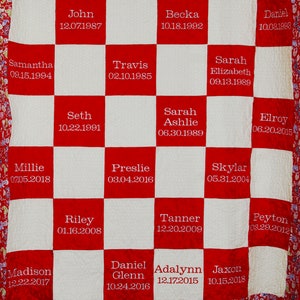 May include: A red and white quilt with names and dates embroidered on each square. The quilt is made of a soft, quilted fabric and has a paisley border.