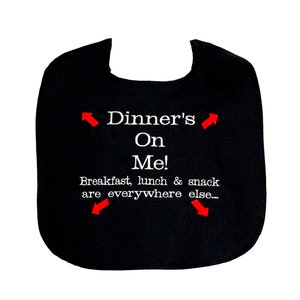 May include: Black baby bib with the text "Dinner's On Me!" in white, along with the phrase "Breakfast, lunch & snack are everywhere else..." Red arrows point to the text. A fun and practical accessory for mealtime.
