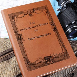 Peut inclure: Un journal relié en cuir marron avec un motif gravé. Le journal porte le titre "The Unpublished Works of" et un espace pour un nom.