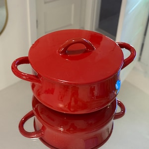 Könnte beinhalten: Ein roter Keramiktopf mit Deckel und zwei Griffen. Der Topf ist auf einem anderen roten Keramiktopf mit zwei Griffen gestapelt.