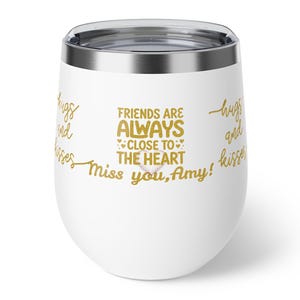 May include: A white stainless steel tumbler with a metallic gold script and block text that reads: FRIENDS ARE ALWAYS CLOSE TO THE HEART, with small heart icons and the phrases hugs and kisses and Miss you, Amy! printed around the exterior.