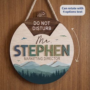 May include: A circular wooden door sign with a rope hanger featuring the text DO NOT DISTURB, Mr. STEPHEN, and MARKETING DIRECTOR. The design includes a mountain and forest landscape in shades of blue and green, with small bird silhouettes.