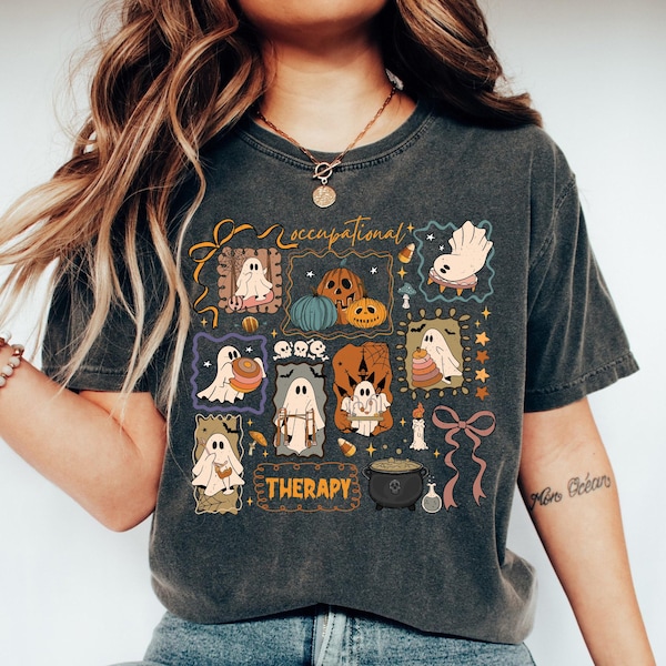Può includere: T-shirt grigio scuro con grafica a tema Halloween. Il design include fantasmi dei cartoni animati, zucche e le parole "Occupational Therapy" in stile vintage. La maglietta ha girocollo e maniche corte.