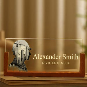 Peut inclure: Plaque de bureau personnalisée avec une base en bois et un panneau en acrylique transparent. Le panneau présente une silhouette de tête de travailleur de la construction remplie d'un design de paysage urbain. Le nom "Alexander Smith" et le titre "CIVIL ENGINEER" sont affichés.