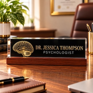 May include: A rectangular desk nameplate featuring a clear acrylic block with a black background, a gold wireframe brain illustration, and the text DR. JESSICA THOMPSON PSYCHOLOGIST in gold lettering, set on a dark wooden base.