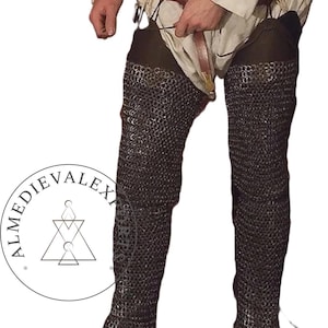 May include: Full-length chainmail leggings, a medieval garment, are the primary focus. The leggings are made of small, interlocking metal rings, offering flexible protection. The image also shows a person wearing a white tunic and holding a brown belt.