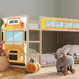 May include: A wooden bunk bed featuring a yellow school bus design on the headboard and footboard. The headboard displays the text "JOHN'S BUS". The room is decorated with soft toys, a pumpkin, and an elephant-shaped toy.