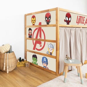 May include: A wooden bed frame featuring cartoon superhero characters such as Iron Man and Captain America. The bed has a beige background with the Avengers logo and a tan curtain. A small stool and basket are nearby.