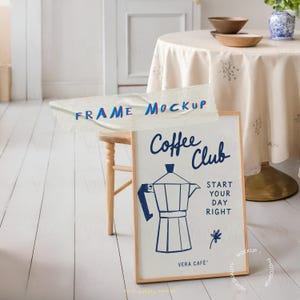 May include: A framed print with the words "Coffee Club" and "Start Your Day Right" in navy blue. The print features a navy blue coffee maker illustration and a small flower. The frame is a light wood colour.