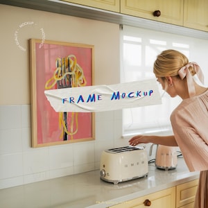 Puede incluir: Una obra de arte enmarcada con un fondo rosa y un diseño de tenedor de espaguetis amarillo y negro. Una tostadora color crema y una tetera rosa están en la encimera. El texto "FRAME MOCKUP" está en la imagen.