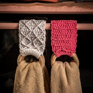 Puede incluir: Dos soportes para pa&ntilde;os de cocina con aros de madera y toallas beige. Un soporte es gris con un patr&oacute;n de diamantes, el otro es rosa brillante. Una calabaza y manoplas para horno est&aacute;n en el fondo.