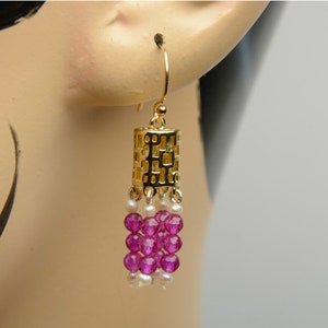 May include: Gold dangle earrings with a geometric design and pink and white beads.