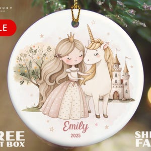 May include: Round ceramic ornament featuring a princess and unicorn illustration. The princess wears a pink dress and crown, standing beside a white unicorn. The ornament includes the name "Emily" and the year "2025". The word "SALE" is in a red banner.