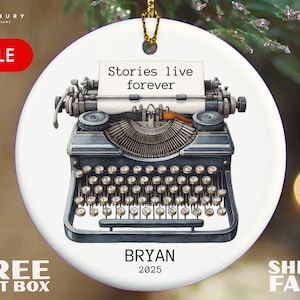 May include: A white ceramic ornament featuring a vintage typewriter illustration. The typewriter has a paper with the text "Stories live forever." Below the typewriter is the name "BRYAN" and the year "2025". A gold-colored string is attached for hanging.
