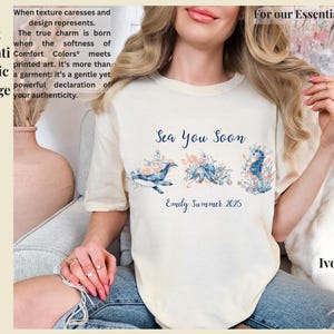 May include: An ivory t-shirt featuring a blue graphic print of a whale, an octopus, and a seahorse surrounded by coral-colored flowers. The text reads Sea You Soon and Emily Summer 2025 in a blue script font across the center of the chest.