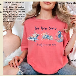 May include: A coral-colored t-shirt featuring a blue graphic of a whale, octopus, and seahorse surrounded by flowers. The text reads Sea You Soon and Emily Summer 2025. The shirt is worn with blue denim jeans. The design is printed with intention.