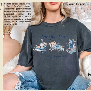 May include: A charcoal gray short-sleeve t-shirt featuring a graphic print of a whale, an octopus, and a seahorse adorned with floral elements. The text "Sea You Soon" and "Emily Summer 2025" is printed in blue script above and below the sea creatures.