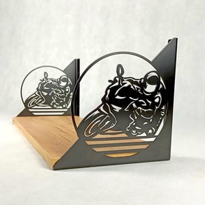 May include: A black metal motorcycle-themed shelf bracket with a wooden shelf. The bracket features a cut-out design of a motorcycle and rider within a circular frame. The shelf is made of light-coloured wood.