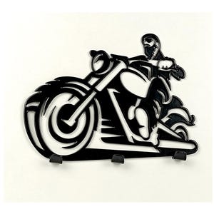 Puede incluir: Llavero de motocicleta de metal negro con una silueta de motorista. El llavero tiene tres ganchos debajo del diseño de la motocicleta. La motocicleta tiene un neumático delantero grande, un faro y un manillar. El diseño está cortado de una sola pieza de metal.