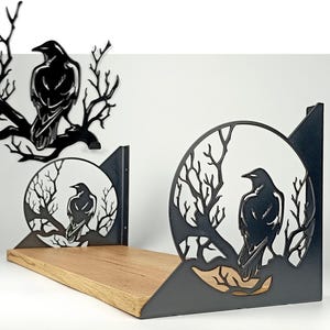 May include: Black metal raven and branch wall decor and shelf. The raven is perched on a branch, with a circular design. The shelf is made of wood and has a black metal support. The decor is suitable for a gothic or nature-themed room.