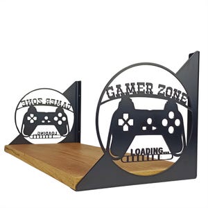 May include: A black metal Gamer Zone shelf with a wooden shelf. The shelf features a cut-out design of a game controller and the words "Gamer Zone" and "Loading...". The shelf is designed to hold video game consoles and accessories.