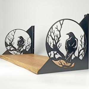 May include: A black metal shelf with a raven silhouette design. The raven is perched on a branch within a circular frame, with a wooden shelf base. The shelf is a decorative item for home decor.