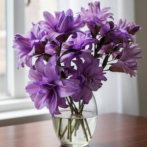 May include: A clear, rounded glass vase filled with water and a bouquet of vibrant purple flowers. The flowers have multiple layers of petals and are arranged to create a full, lush display. The vase sits on a wooden surface.