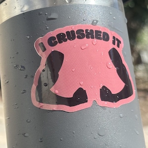 May include: A gray water bottle with a pink and black sticker that says "I Crushed It".