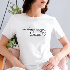 Op de afbeelding: Wit T-shirt met de tekst "as long as you love me" in zwart script, gevolgd door een hartsymbool. Het shirt heeft korte mouwen en lijkt gemaakt van een zacht materiaal.