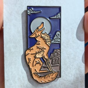 Night Laughter - Enamel pin with a coyote laughing howling at the moon with cliffs in the background