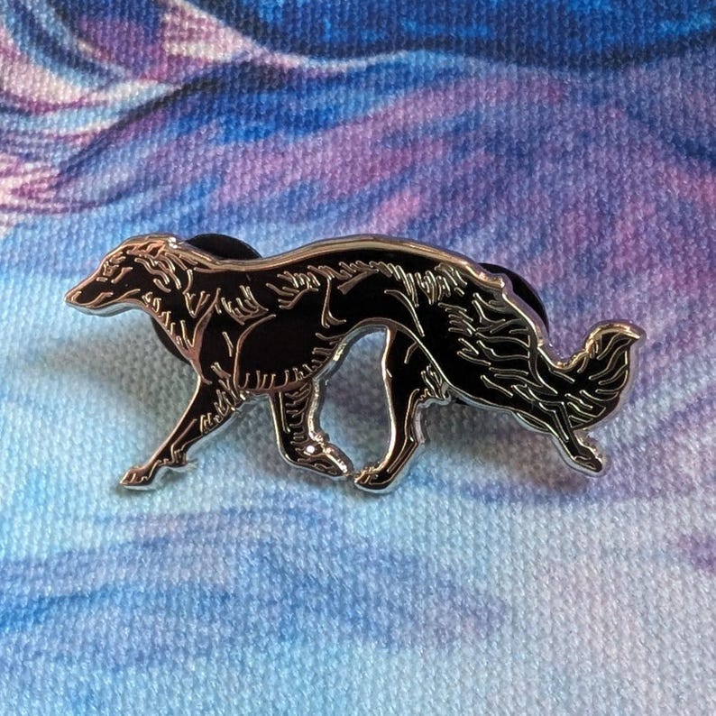 K&ouml;nnte beinhalten: Ein schwarz-silberner Emaille-Pin mit einem stilisierten Borzoi-Hund in einer Laufpose. Der Pin hat eine gl&auml;nzende silberne Umrandung und ein schwarzes Innenteil, vor einem blau-violetten Hintergrund.
