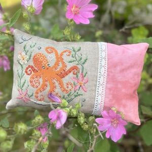 May include: A hand-stitched cushion featuring an orange octopus surrounded by flowers. The cushion is made of linen and has a pink cotton back.
