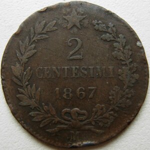 Puede incluir: Una moneda redonda y desgastada de color cobre que muestra el número 2 sobre el texto CENTESIMI y el año 1867. Una estrella de cinco puntas se sitúa en la parte superior, mientras una corona de hojas atada con un lazo enmarca el texto.