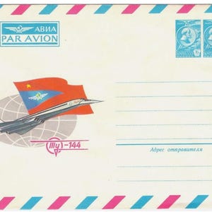 Pode incluir: Um envelope branco com uma borda listrada rosa e azul. O envelope tem um avião vermelho, branco e azul com uma bandeira vermelha com uma estrela e um emblema azul. O texto "AVIA PAR AVION" está impresso em preto no topo do envelope. O texto "Ил-144" está impresso em preto na parte inferior do envelope. O texto "Адрес отправителя" está impresso em azul na parte inferior do envelope.