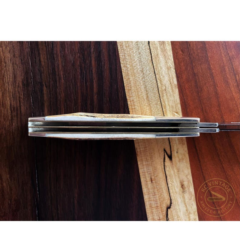 Puede incluir: Un cuchillo de bolsillo vintage cerrado, con mango de hueso y hoja de acero inoxidable. El mango muestra una textura. El fondo es una superficie de madera con patrones marr&oacute;n oscuro y marr&oacute;n claro.