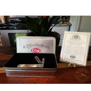 Puede incluir: Una navaja de bolsillo vintage con mango de hueso, exhibida en una caja met&aacute;lica. La caja est&aacute; marcada con "W.R. Case & Sons Cutlery Co." y "Hand Crafted Knives Since 1889." Tambi&eacute;n hay un certificado de autenticidad.