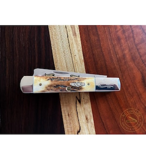 Puede incluir: Una navaja de bolsillo vintage con una hoja de acero inoxidable y un mango con un patr&oacute;n crema y marr&oacute;n. La navaja tiene el texto "1981" y "L9200" grabado en la hoja y el mango. La navaja se muestra sobre una superficie de madera.