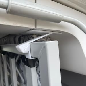 Può includere: Una scala pieghevole in metallo bianco con un fermo in plastica bianca. La scala è fissata a un soffitto bianco.