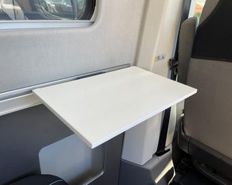 May include: A white folding table mounted to the wall inside a vehicle. The table is made of a smooth, white material and is attached to a white support post.