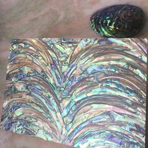 May include: A rectangular sheet of iridescent abalone shell inlay featuring a swirling, multi-colored pattern of blues, greens, and purples, accompanied by a single, rounded, polished abalone shell piece with similar vibrant, shimmering colors.