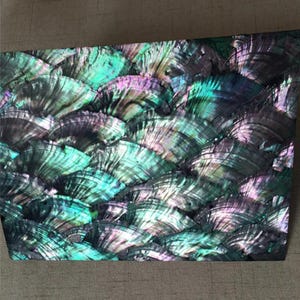 May include: A rectangular panel featuring a dense, overlapping mosaic of iridescent abalone shell fragments. The surface displays a vibrant spectrum of deep emerald green, teal, and violet hues, with a high-gloss finish that reflects light.