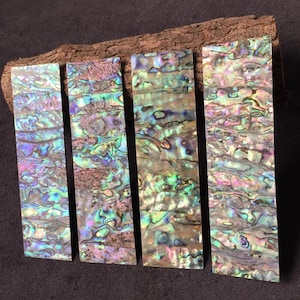 Könnte beinhalten: Vier rechteckige Einlagestreifen aus Abalone-Muschel mit einer lebendigen, irisierenden Oberfläche und wirbelnden Mustern in Grün, Blau, Rosa und Violett. Jedes Stück zeigt eine natürliche, schimmernde Perlmutttextur mit einzigartigen Farbvariationen.
