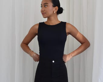 Puede incluir: Una mujer con un top negro sin mangas y pantalones negros. Está de pie frente a un fondo blanco.