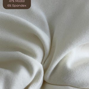 Puede incluir: Primer plano de una tela blanca de canal&eacute; con el texto "47% Algod&oacute;n 47% Modal 6% Spandex".