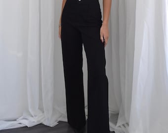 Puede incluir: Una mujer con un top negro sin mangas y pantalones negros de pierna ancha. Los pantalones tienen cintura alta y pierna recta.