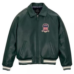 Puede incluir: Una chaqueta de cuero verde oscuro con cremallera frontal completa, cuello cl&aacute;sico y pu&ntilde;os y dobladillo acanalados con rayas blancas. Un parche en el pecho izquierdo muestra el texto AVIREX con un gr&aacute;fico de escudo que contiene estrellas.