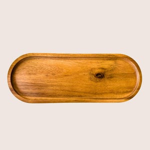 May include: An oval wooden serving tray. The tray is made from light brown wood, displaying a natural wood grain. It features a raised edge and a smooth surface. The tray is ideal for serving food.